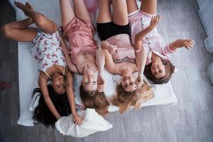 Having a good time. Inverted portrait of charming girls that lying on bed in nightwear. Top view photo