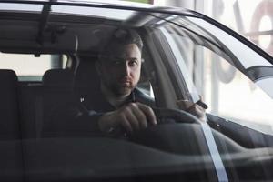 Having busy day. Front view of young bearded businessman sitting in his luxury black car photo