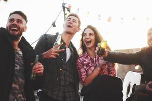 Gesturing and smiling. Group of young cheerful friends having fun while takes selfie on the roof with decorate light bulbs photo