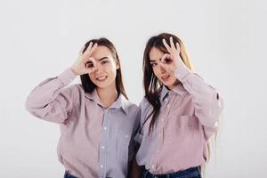 Playful mood. Two sisters twins standing and posing in the studio with white background photo