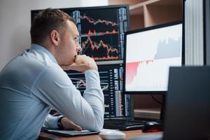 Thinks what to do next. Man working online in the office with multiple computer screens in index charts photo