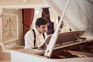 Beautiful man. Young professional musician in official clothes plays on the white piano