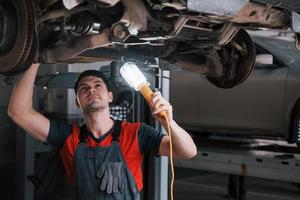 Professional in action. Man at the workshop in uniform fixes broken parts of the modern car photo