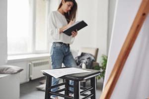 Ordinary workday of art designer. Young brunette in the room with white walls and daylight that comes from the window photo