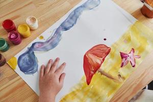 Picture of beach with sand, star and clouds. Little girl is drawing by using gouache and brush. Learning in the art class photo