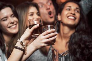 juventud activa. gente feliz bailando en el club nocturno de lujo junto con diferentes bebidas en sus manos foto