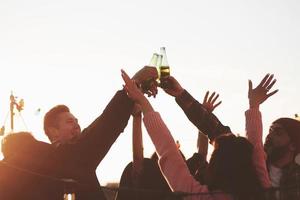 Ready for the party. Holidays on the rooftop. Cheerful group of friends raised their hands up with alcohol photo