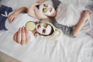 Simple but effective way. Girl holds cucumber ring in the hand. Lying on the white bed. Top view. Conception of skin care photo