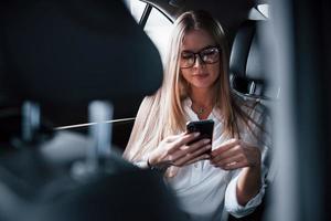 Internet está en todas partes. mujer de negocios inteligente se sienta en el asiento trasero del coche de lujo con interior negro foto