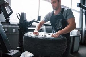 Pulling it off. Young man works with wheel's disks at the workshop at daytime photo