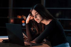 Wanna go home. Attractive brunette businesswoman works alone in the office at nightime photo