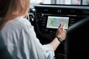 Technologies makes life much easier. Beautiful blonde girl sitting in the new car with modern black interior photo