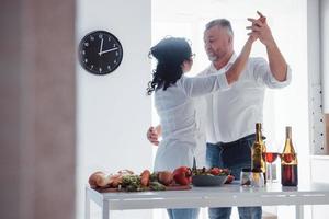 They knows some dance moves. Senior man and his wife in white shirt have romantic dinner on the kitchen photo