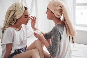 Helps each other. Conception of skin care by using white mask on the face. Two female sisters have weekend at bedroom photo