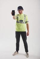 Smartphone in the hand. Policeman in green uniform stands against white background in the studio photo