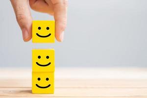 Hand holding smile face symbol on yellow wooden cube blocks. Emotion, Service rating, ranking, customer review, satisfaction and feedback concept photo