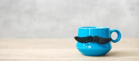 Blue coffee cup or tea mug with Black mustache decor on table. Blank copy space for text. Blue November, Happy Father day and International men day concept photo