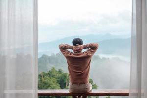 happy tourist man relaxing and looking mountain view at countryside home or homestay in the morning. Vacation, blogger, SoloTravel, journey, trip and relaxing concept photo