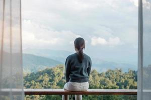Happy woman relaxing and looking mountain view at countryside home or homestay in the morning. Vacation, blogger, SoloTravel, journey, trip and relaxing concept photo