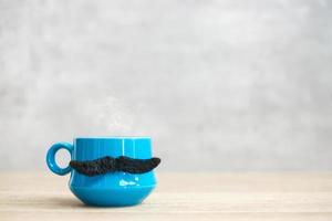 Blue coffee cup or tea mug with Black mustache decor on table. Blank copy space for text. Blue November, Happy Father day and International men day concept photo