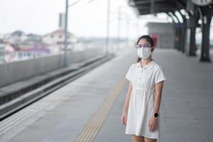 mujer con mascarilla protectora prevención coronavirus y contaminación pm 2.5 durante el tren de espera. transporte público. seguridad bajo la pandemia de covid-19 y el polvo foto