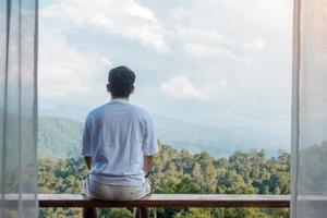 Happy tourist man relaxing and looking mountain view at countryside home or homestay in the morning. Vacation, blogger, SoloTravel, journey, trip and relaxing concept photo