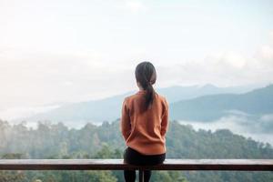 Happy woman relaxing and looking mountain view at countryside home or homestay in the morning. Vacation, blogger, SoloTravel, journey, trip and relaxing concept photo