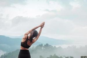 Young woman doing Yoga and stretching muscle in morning, healthy girl meditation against mountain view. wellness, fitness, Vitality, exercise and work life balance concepts photo