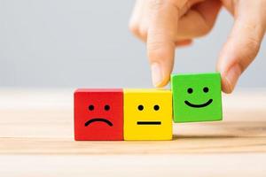 Hand holding Emotion face symbol wooden cube blocks. Service rating, ranking, customer review, satisfaction and feedback concept photo