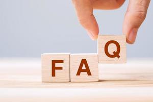 Hand holding wooden cube blocks with FAQ text  on table background. Financial, marketing and business concepts photo