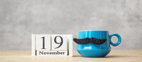 día internacional del hombre con calendario del 19 de noviembre, taza de café azul o taza de té y decoración de bigote negro en la mesa. feliz día del padre y concepto de celebración