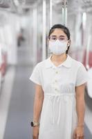 mujer con mascarilla médica y escuchando música con auriculares en el tren. transporte público y seguridad bajo la pandemia de covid-19 foto