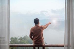 happy tourist man relaxing and looking mountain view at countryside home or homestay in the morning. Vacation, blogger, SoloTravel, journey, trip and relaxing concept photo