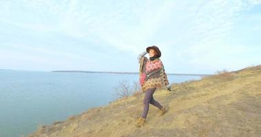yong hipster donna viaggiatore con cappello e poncho che cammina all'aperto nelle montagne vicino al lago video