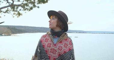 yong hipster donna viaggiatore con cappello e poncho che cammina all'aperto nelle montagne vicino al lago video