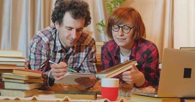 Ungt par studerar hemma med många böcker och dator video