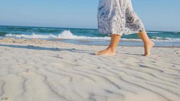 giovane bella donna vestita con un abito bianco cammina a piedi nudi sulla spiaggia estiva video