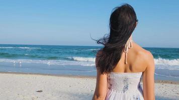 Young beautiful woman dressed in a white dress walk barefoot on the summer beach video