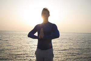 Portrait of young man meditating on the beach, sunrise background photo