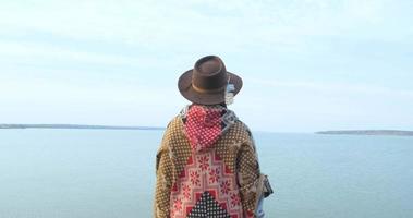 yong hipster donna viaggiatore con cappello e poncho che cammina all'aperto nelle montagne vicino al lago video