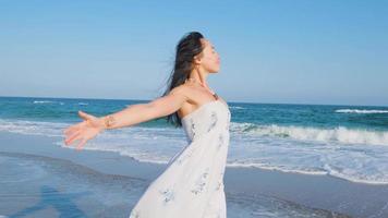 giovane bella donna vestita con un abito bianco cammina a piedi nudi sulla spiaggia estiva video