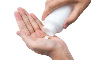 Adult woman hand pouring tablets pills out of white plastic bottle in to her hand isolated on white background. Health care in adult people photo