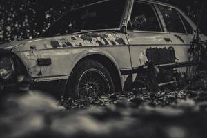 Old wrecked car in black and white scene. Abandoned rusty car in the forest on bokeh background. Decayed and rusty wrecked abandoned car. The art of abandoned used car. Tragedy and loss. Sadness photo