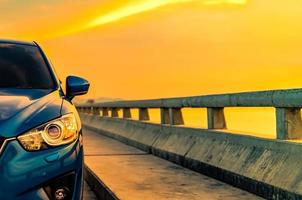 Luxury blue SUV car with sport and modern design parked on concrete road by the sea at sunset. Hybrid auto and automotive concept. Road trip and car driving for travel. Electric car technology concept photo