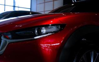 Closeup headlight of shiny red luxury SUV car in showroom. Elegant electric car with sport design. Car parked in showroom. Car dealership. Electric vehicle development concept. Future transportation. photo