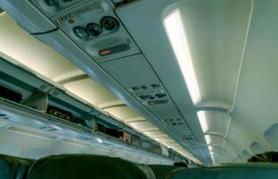 Selective focus on overhead reading light in commercial airplane on blurred overhead bin with opened door show carry on in overhead stowage. Airplane interior. Inside of commercial airline. photo