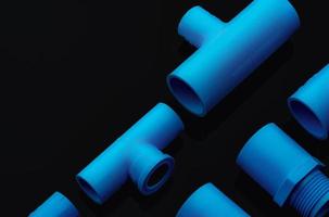 Set of blue PVC pipe fittings isolated on dark background. Blue plastic water pipe. PVC accessories for plumbing. Plumber equipment. Bend and three way connection plastic pipe for water drain sewage. photo
