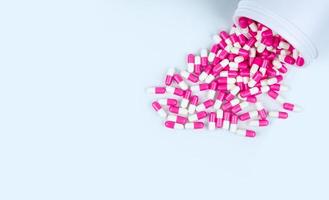 Pink-white antibiotic capsule pills spread out of white plastic drug bottle. Antibiotic drug resistance concept. Antibiotic drug use. Global healthcare. Pharmacy background. Pharmaceutical industry.