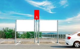 Car parking space and empty advertising board near the sea, mountain and concrete bridge. White car driving on asphalt road in parking lot area for rental service zone A. Automotive industry. photo