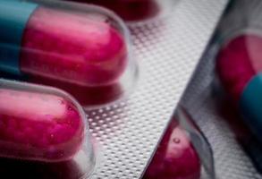 Selective focus of blue, pink capsule with granule in side pills. Pills in blister pack on white background. Pharmaceutical dosage form and packaging. Anti-fungal medicine. photo